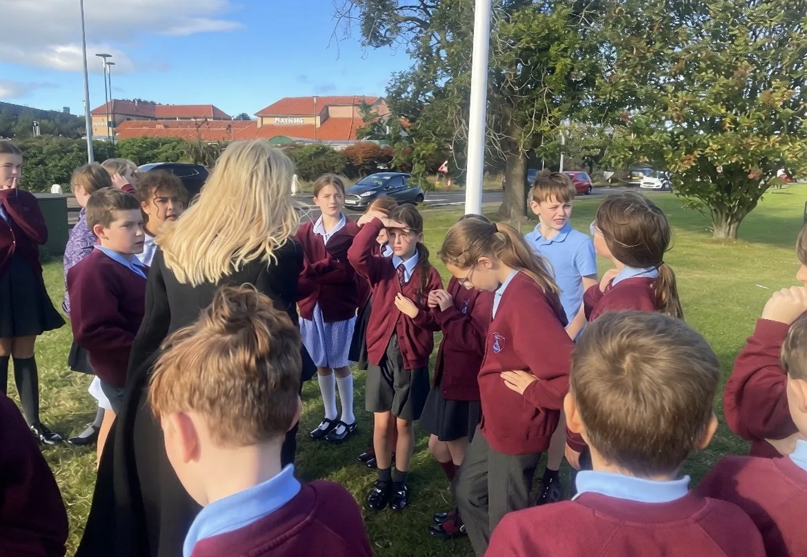 Holy Trinity School pupils in maroon jumpers gathered on the grass at Newfields