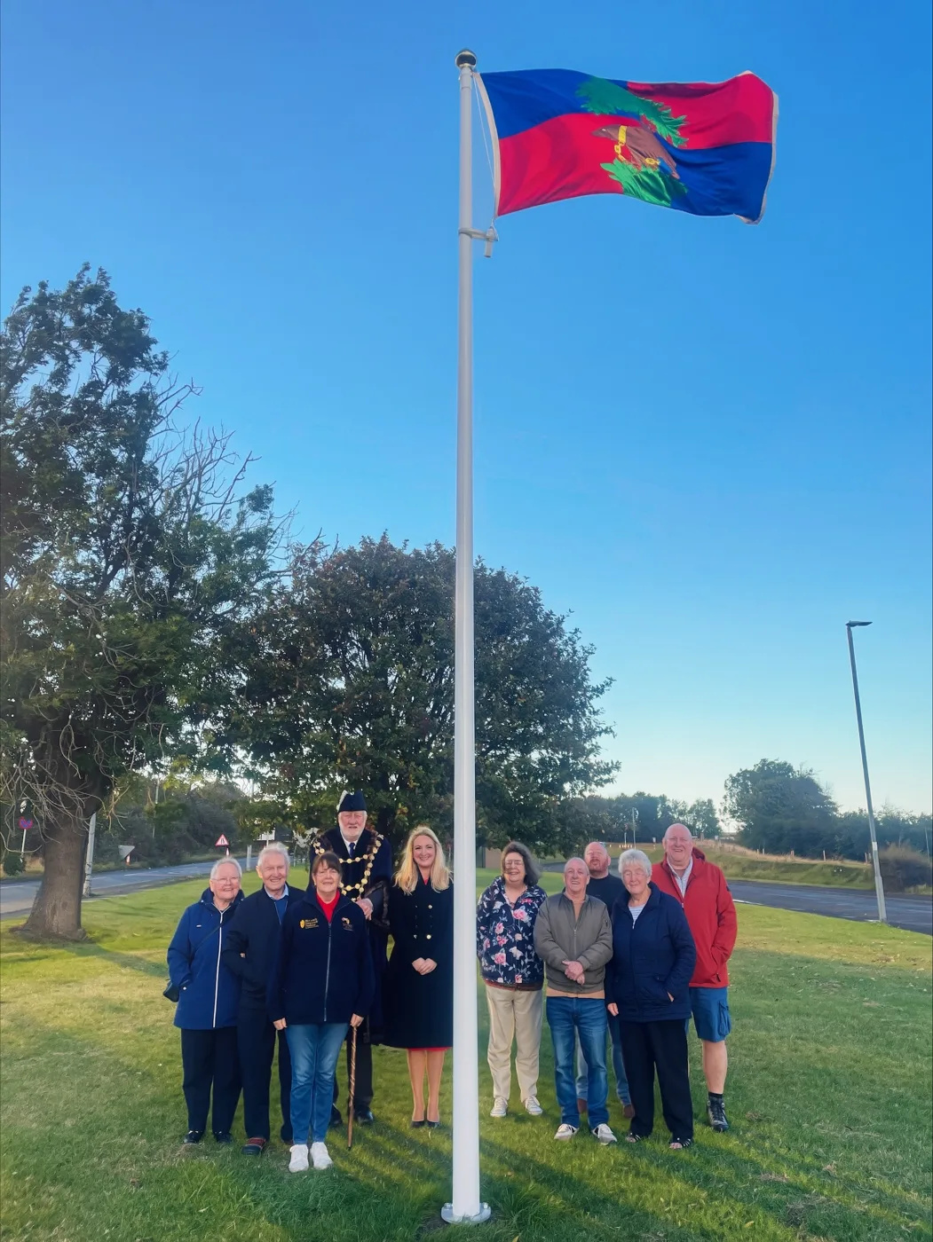 A group of adults standing beneath the Berwick flag on a tall white pole at Newfields